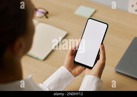 High angle closeup of young woman holding smartphone with white screen mockup at workplace Stock Photo