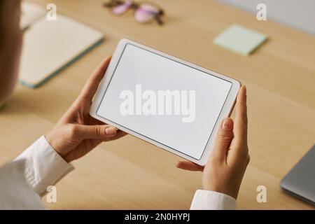 Closeup of young woman holding tablet with white screen mockup at workplace Stock Photo