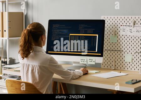 Back view of female programmer writing code while working at desk, copy space Stock Photo