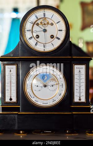 Vintage table clock with white deal, retrograde calendar, moon phase indicator, Reaumur and Celsius temperature scales. Close up frontal photo Stock Photo