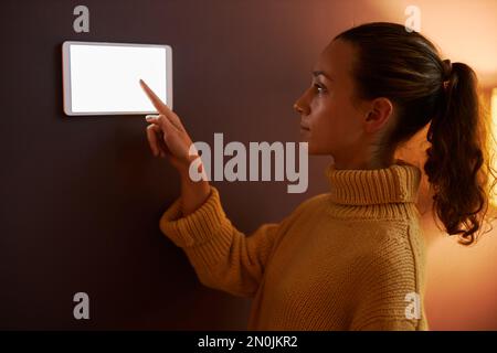 Side view portrait of young woman using digital control panel on wall at home Stock Photo