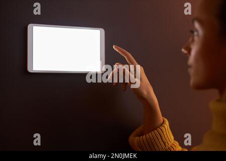 Closeup of young woman using digital control panel with blank screen on wall at home Stock Photo