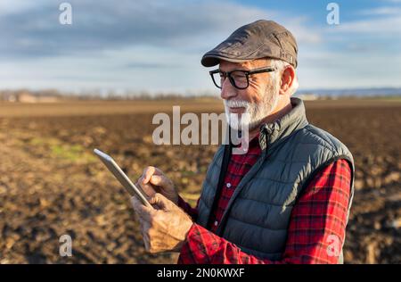 Senior farmer smiling and holding tablet in field in autumn time Stock Photo