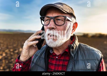 Excited mature farmer talking on mobile phone in field Stock Photo