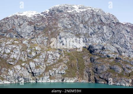 The springtime view of a steep rocky shore and a small waterfall in Glacier Bay national park (Alaska). Stock Photo