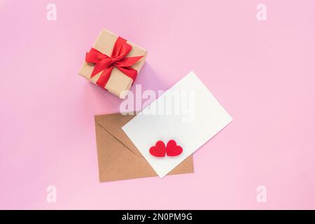 Blank paper and envelope with two red hearts and gift box on pink background. Top view, flat lay, mockup. Valentines day concept. Stock Photo
