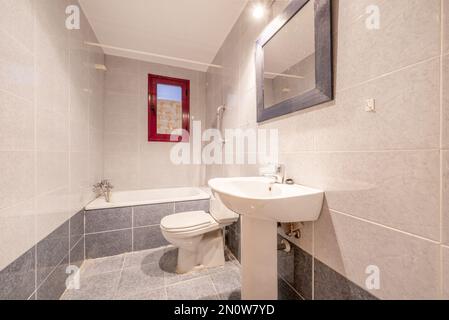 bathroom with bathtub, mirror with rectangular frame attached to the wall, two-tone tiles and white toilets Stock Photo