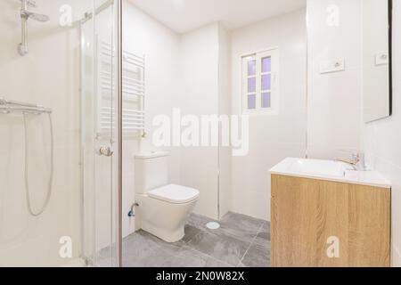 bathroom with a wooden sink below a frameless wall-hung mirror, a walk-in shower with screens, a heated towel rail and white wooden doors Stock Photo