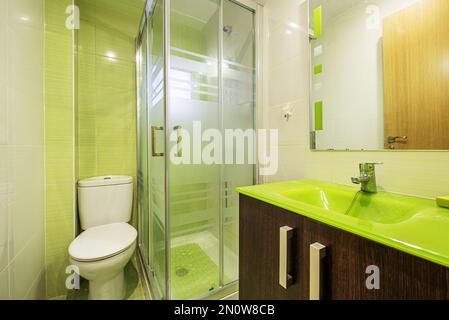 Bathroom with dark wood cabinet, pistachio green glass sink, mirror with sconces and small square shower cubicle with glass partitions Stock Photo