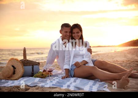 Lovely couple having romantic picnic on beach at sunset Stock Photo