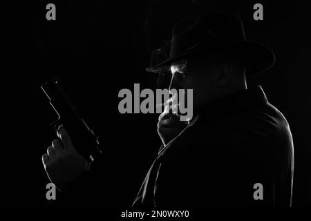 Old fashioned detective with gun smoking cigarette on dark background, black and white effect Stock Photo