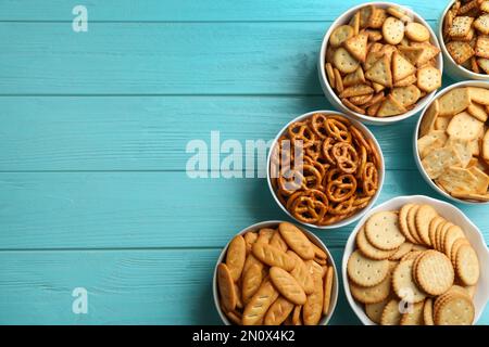 Different delicious crackers in bowls on turquoise wooden table, flat lay. Space for text Stock Photo