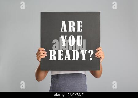 Man holding poster with text Are You Ready? on light grey background Stock Photo