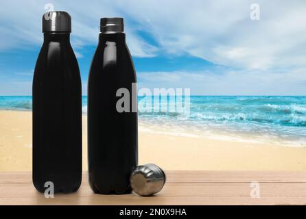 Thermo bottles on wooden table near sea under blue sky Stock Photo