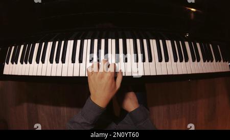 The student is learning to play the piano. A man with two hands plays a beautiful piano in the classroom close-up. Shot with a wide angle camera. Fish Stock Photo