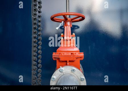 Red water valve on the side of a blue water tank. Stock Photo