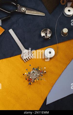 Tailor workplace accessories. Close up view of the eco leather and sewing equipment laying on the table. Set of pins, bobbin for a sewing machine Stock Photo