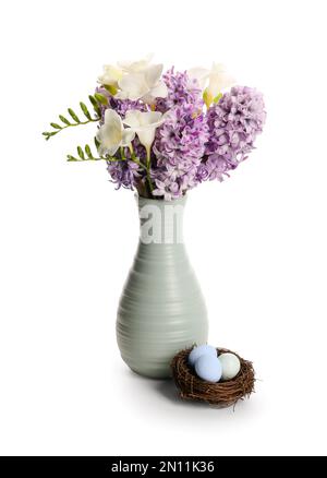 Vase with beautiful spring flowers and nest of Easter eggs on white background Stock Photo