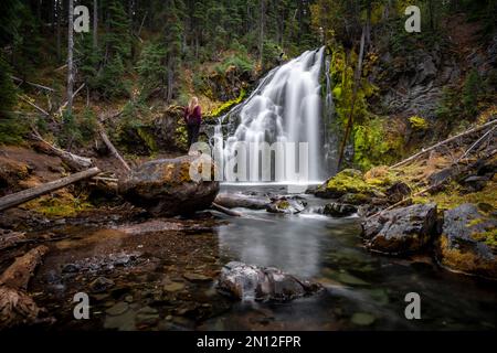 Young woman standing on stone, waterfall, Middle Tumalo Falls, long exposure, Tumalo Creek, Bend, Deschutes County, Oregon, USA, North America Stock Photo