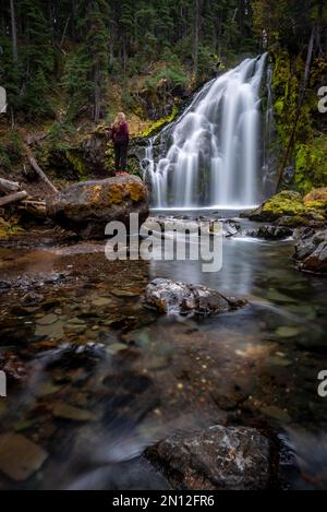 Young woman standing on stone, waterfall, Middle Tumalo Falls, long exposure, Tumalo Creek, Bend, Deschutes County, Oregon, USA, North America Stock Photo