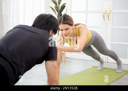 Young woman and man practicing workout with posing plank on mat while motivation and determined at home, female and male doing weight training with st Stock Photo