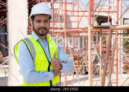 Portrait of young man is engineer wearing helmet smile with satisfied at construction site, architect or contractor standing and thumbs up with confid Stock Photo
