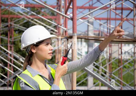 Young woman engineer using radio command with worker in construction site, architect or contractor speak to radio for control and planning development Stock Photo