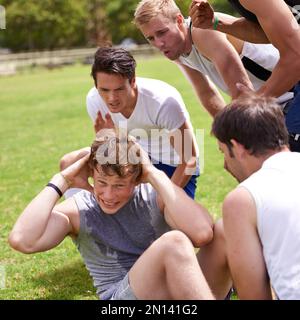 Come on, buddy. a young man doing sit-ups while his friends are cheering him on. Stock Photo