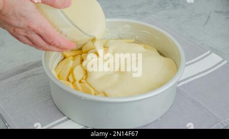 Chef pouring cake batter into a baking pan on the top of apple slices. Apple cake preparation process, recipe Stock Photo