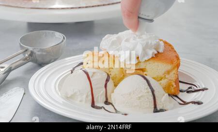 Slice of a freshly baked apple cake with whipped cream topping, served with vanilla ice cream and chocolate close-up on a white plate Stock Photo