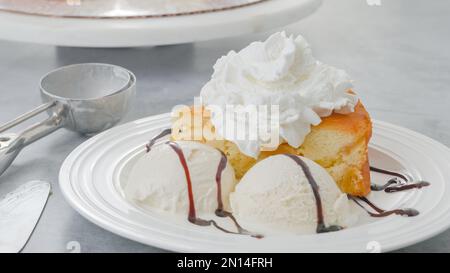 Slice of a freshly baked apple cake with whipped cream topping, served with vanilla ice cream and chocolate close-up on a white plate Stock Photo