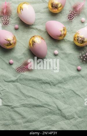 Easter eggs are painted with gold and violet paint on a green linen background. Concept of Easter holidays. Festive background. Stock Photo