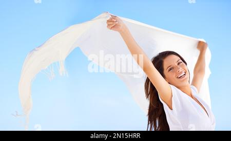 Without a care in the world...A beautiful young woman holding a white sarong thats blowing in the wind. Stock Photo
