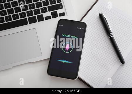 Smartphone with activated voice search app, laptop and stationery on white table, flat lay Stock Photo