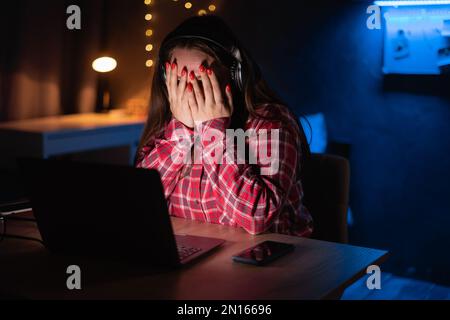 Young female watching scary movie, hiding face in fear. Horror movie at home. Online film service Stock Photo