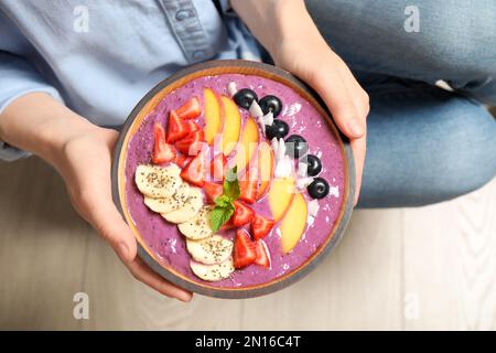 Woman holding bowl with tasty acai smoothie and fruits, top view Stock Photo