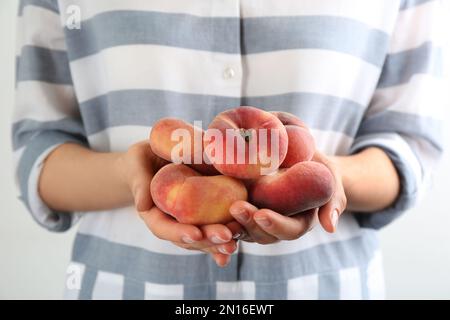 Woman holding heap of fresh ripe donut peaches on light background, closeup Stock Photo