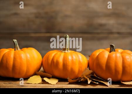 Ripe orange pumpkins and autumn leaves on wooden table. Space for text Stock Photo