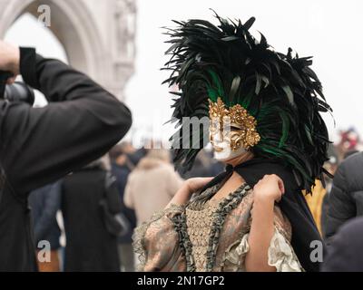 Vinece carnival. A woman in a vintage costume, wearing a carnival mask bordered by a circle of high black feathers, poses to a photographer Stock Photo