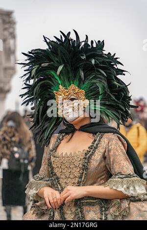 Vinece carnival. A woman in a vintage costume with a lace, wearing a golden carnival mask bordered by a circle of high black feathers, stands alone Stock Photo