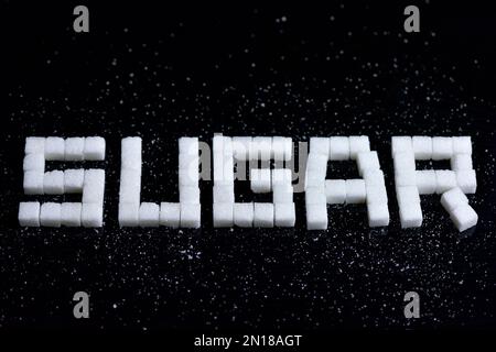 High angle shot of a sugar cubes on a black background. where you can read the message Sugar. selective focus. Stock Photo