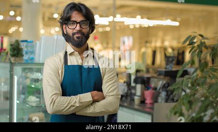 Successful small business owner bearded Indian Arabian man in eyeglasses standing in cafeteria restaurant showing ok gesture smile. Male cafe waiter Stock Photo