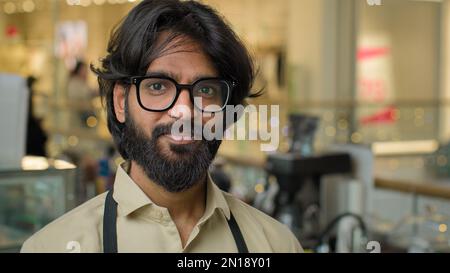 Successful small business Indian Arabian ethnic owner bearded man wearing eyeglasses standing in workplace cafeteria restaurant. Portrait of Stock Photo
