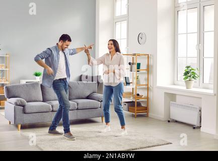 Happy laughing young couple having fun dancing at home in living room. Stock Photo