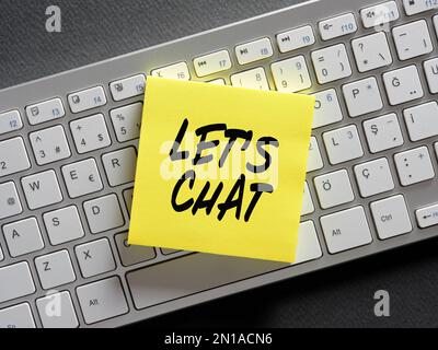 Online computer chatting concept. The word let's chat written on a sticky note paper on computer keyboard. Stock Photo