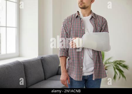 Young Caucasian man with broken wrist wears arm sling bandage on his injured hand. Stock Photo