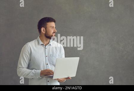Portrait of a pensive male IT programmer standing pensively with a laptop in his hands. Stock Photo