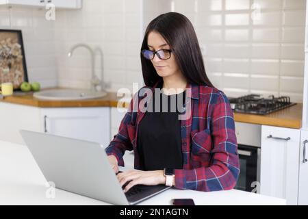 Young white woman with brown hair working on laptop computer at home. Focused freelancer female typing text on modern notebook pc Stock Photo