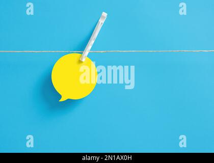 Blank yellow speech bubble attached on a clothesline with a clothespin on blue background. Stock Photo