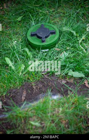 A anti-tank green mine lies on the ground camouflaged in green grass. Weapon bomb anti-personnel mine. Projectile of war. Outdoors. War ammunition, anti tank bomb, combat, soldier equipment Stock Photo